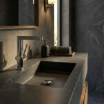 Minimalist bathroom design featuring the Finoris 230 basin mixer on a dark grey Corian countertop with a classic chrome drain and wooden interior accents under natural sunlight