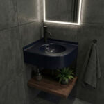 A contemporary bathroom corner featuring a curved corner sink made from Deep Night Sky Corian, showcasing a dark navy surface with white starry speckles. The setup includes a matte black faucet, dark grey stone-textured wall tiles, and a dark wooden floating shelf underneath with towels and a small plant