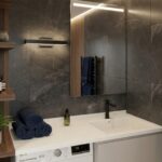 A modern bathroom vanity featuring a white Corian countertop with an integrated sink and black faucet. The counter extends over a washing machine and wooden cabinets. Rolled towels, a potted plant, and a mirror are set against dark grey stone wall tiles