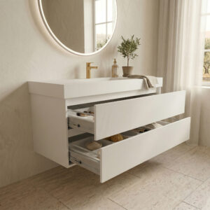 A contemporary, light-filled bathroom featuring a floating white Corian vanity. The seamless white solid surface countertop integrates the sink basin. Below, a full-width drawer is neatly organized with custom white dividers holding makeup brushes, natural sponges, and cosmetic products. On the surface sits a minimalist golden faucet, a terracotta pot with an olive tree, a soap dispenser, and a folded towel. Above, a large round mirror with halo lighting is mounted on a textured plaster wall, with a window and sheer linen curtains to the right. The overall design is clean, organic, and highly organized.